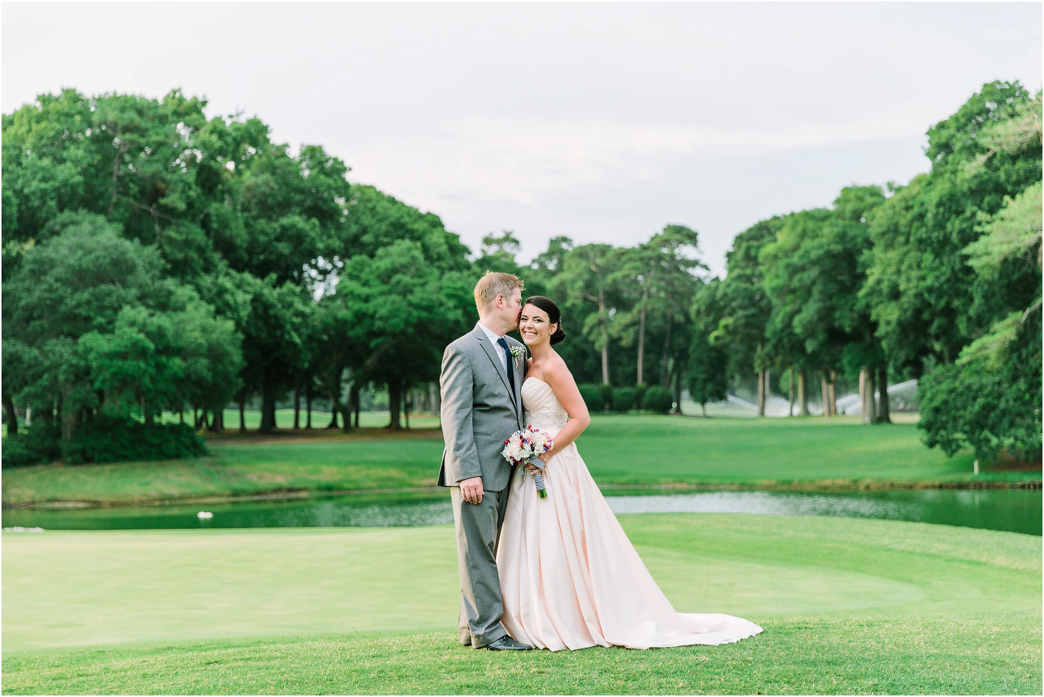 The groom gently kissing his bride on the green