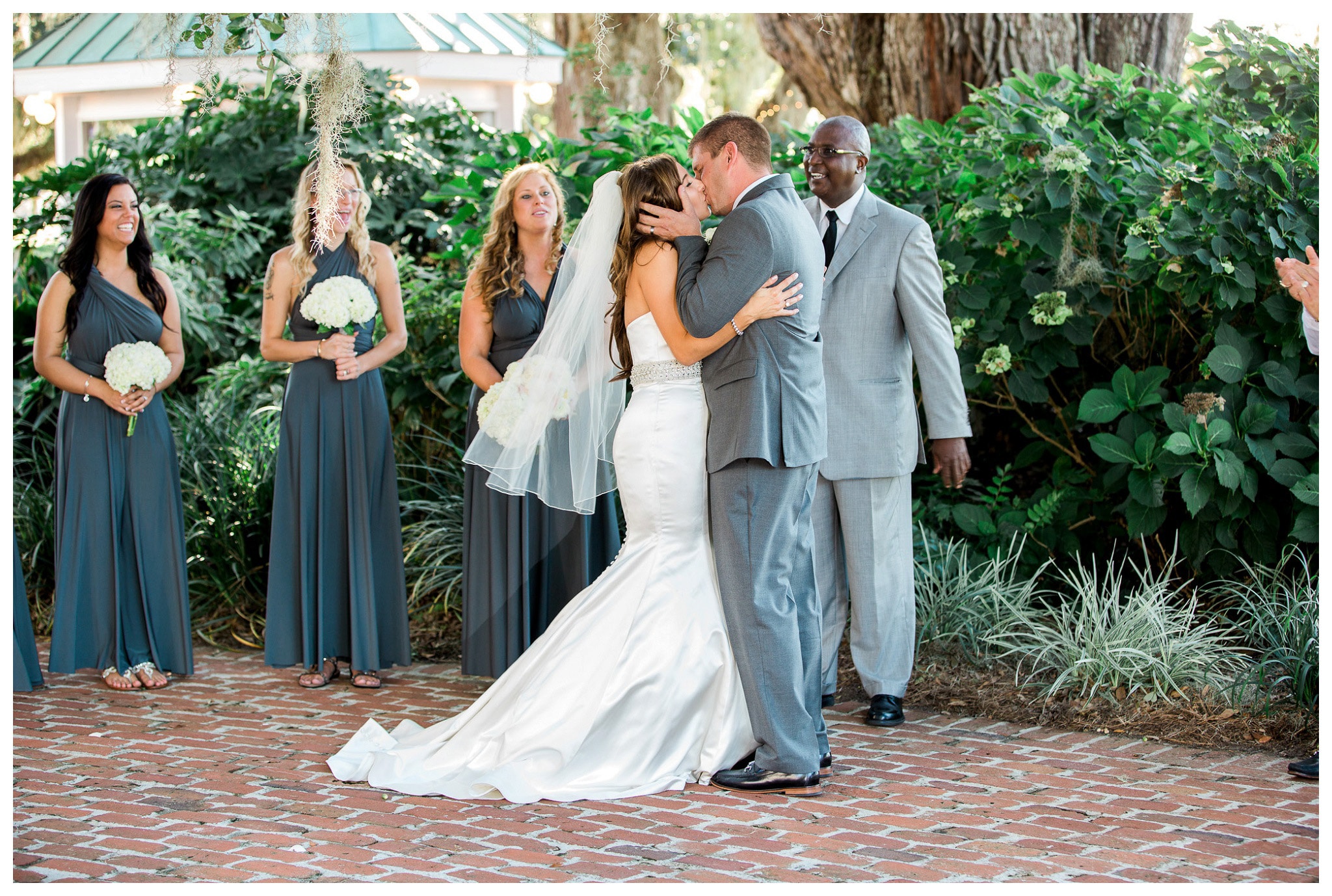 You may kiss the Bride - a passionate kiss while the pastor and bridesmaids look on. Kay and Josh's wedding at the Heritage Plantation, Pawleys Island, South Carolina on September 19, 2015 Heritage Plantation Southern wedding, Pawleys Island, South Carolina Venue and Catering: Heritage Club, Pawleys Island Music: Paul Matthews Entertainment Brides dress: The Little White Dress Cake: Buttercream Cakes and Catering Event Rentals: Eventworks Photographer: One Life Photography