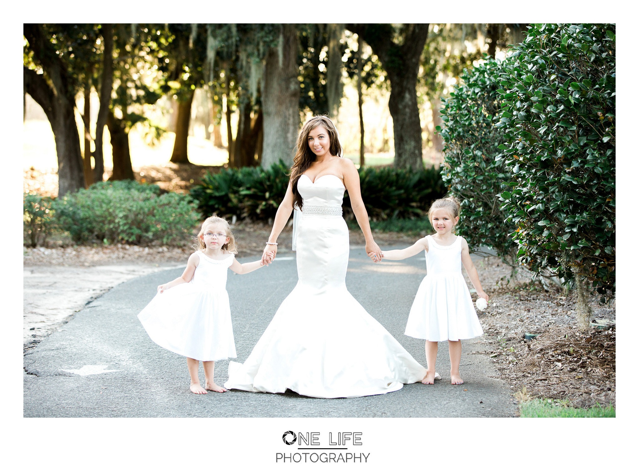 The bride and her flower girls in white on the walkway, Kay and Josh's wedding at the Heritage Plantation, Pawleys Island, South Carolina on September 19, 2015 Heritage Plantation Southern wedding, Pawleys Island, South Carolina Venue and Catering: Heritage Club, Pawleys Island Music: Paul Matthews Entertainment Brides dress: The Little White Dress Cake: Buttercream Cakes and Catering Event Rentals: Eventworks Photographer: One Life Photography
