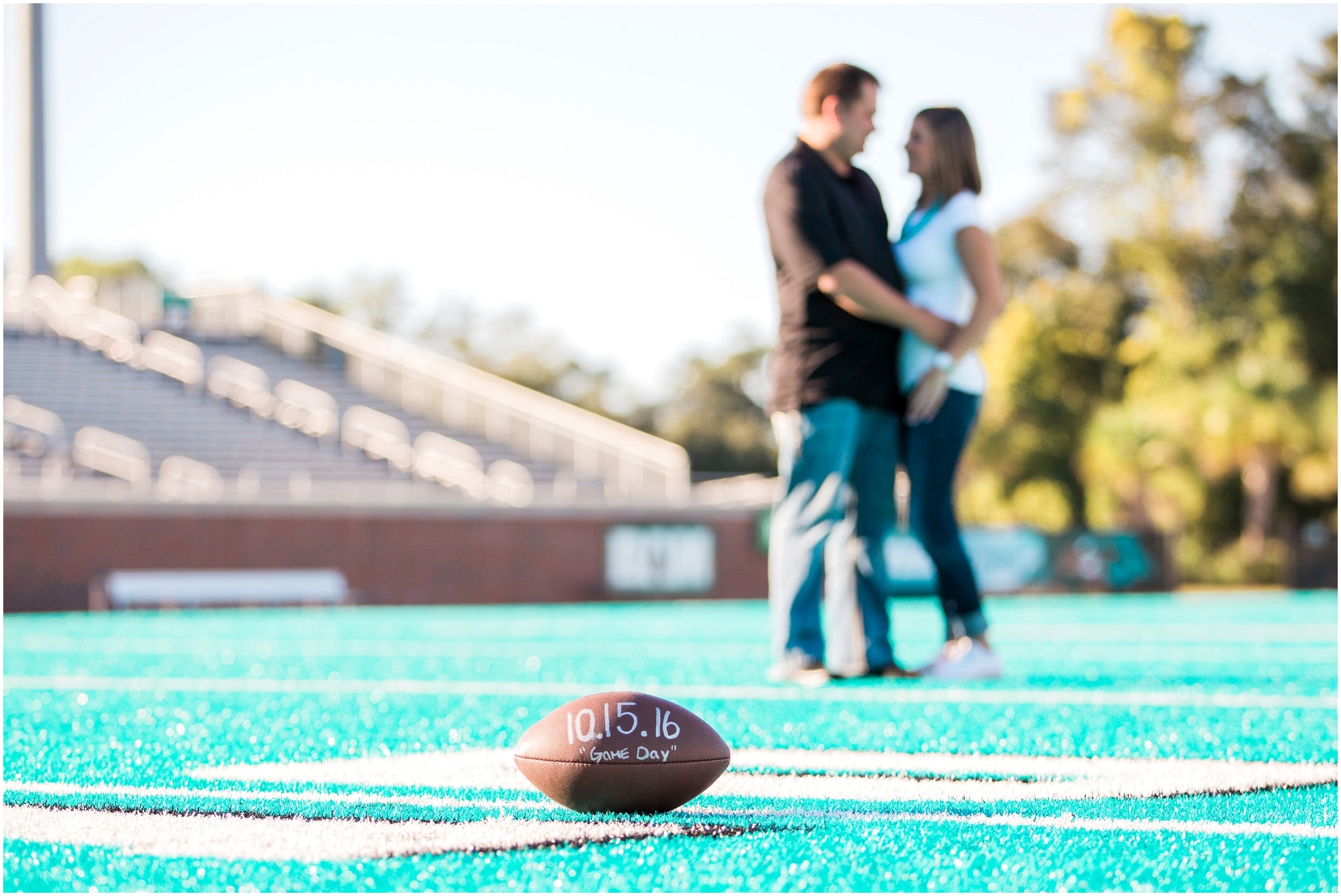 Engagement photography on a football field, Save the Date Football in focus in the foreground, Dana and Bradley out of focus in the background, Myrtle Beach Engagement Photography Session 1, Coastal Carolina University, www.onelifephoto.net