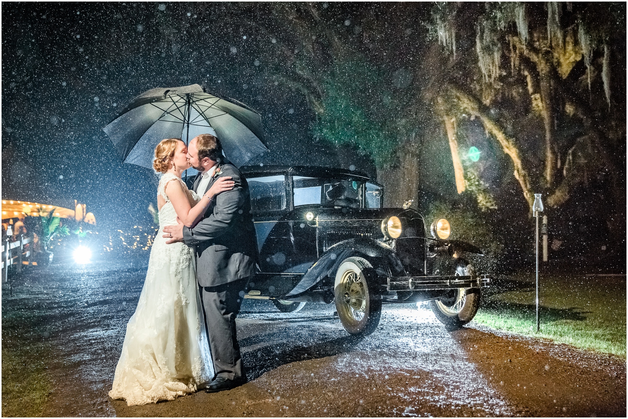 Paige and Dorcey kissing in the rain under an umbrella in front of an old car, Upper Mill Plantation Wedding Session 1, Conway, South Carolina, Wedding coordinator, flowers and Cake - Willow Event Designs, Venue - Upper Mill Plantation, DJ - Carolina Entertainment, Dress - Foxy Lady, www.onelifephoto.net Photography