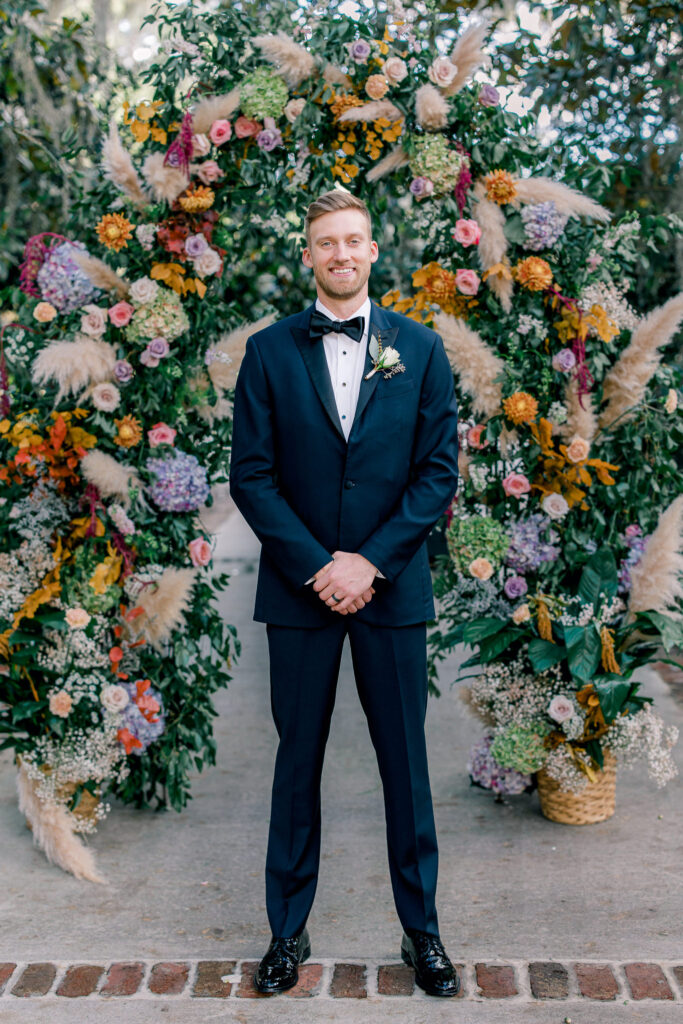 Groom in front of the floral arch